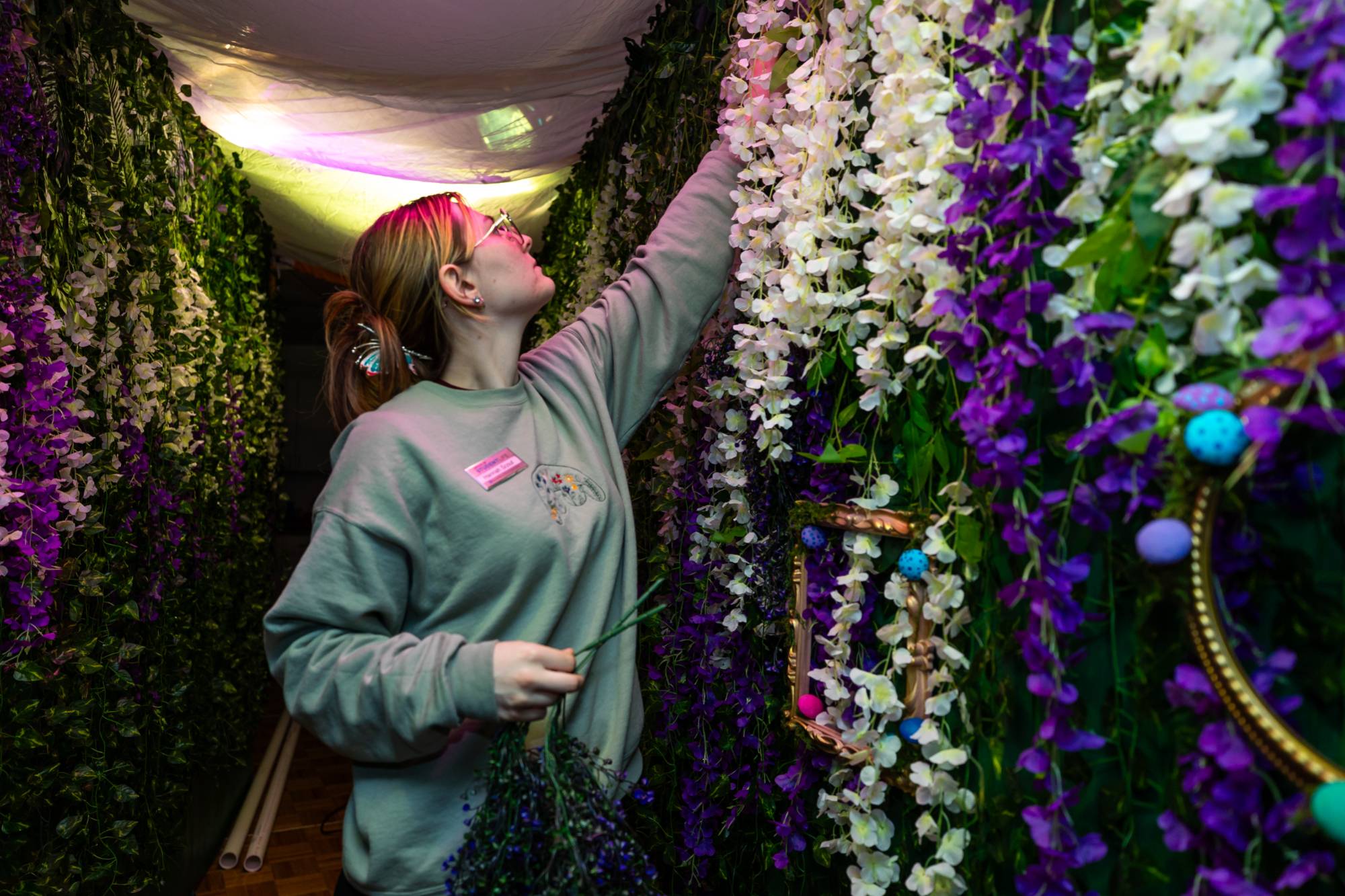 A student staff member adding decorative vines and flowers to the wall of an enchanted forest set